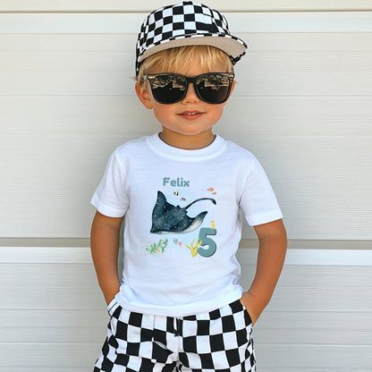 Personalisiertes Geburtstagsshirt für Kinder mit großem Rochen, tropischen Fischen, Algen, Name und Geburtstagszahl. Individuelles Kindergeburtstags-Outfit für Mädchen und Jungen mit Unterwasser-Motiv und Meerestiere-Design. Perfekt als Geburtstags-T-Shirt mit Namen, persönliches Geburtstagsgeschenk für Kinder oder Outfit für Meerjungfrauen-Party, Unterwasserparty oder Ozean-Geburtstag. Personalisierbares Kinder-Shirt mit Rochen, Zahl und Namen. T-Shirt zum Geburtstag für kleine Meeresfans und Ozean-Liebhab