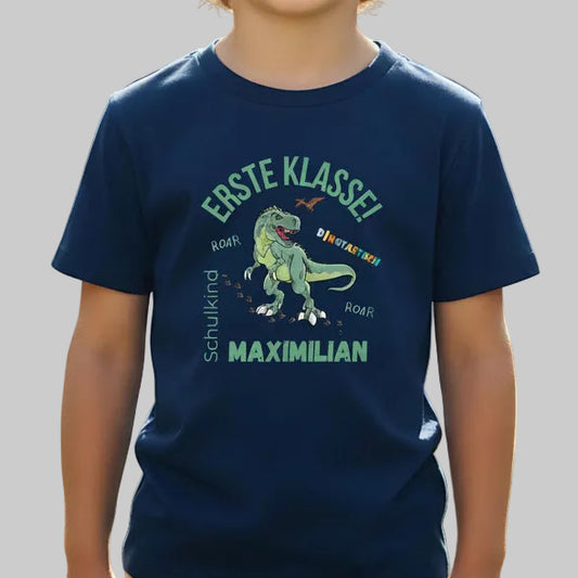 Personalisiertes Schulkind T-Shirt 2026 mit grünem Dinosaurier-Motiv und Spruch „Erste Klasse – Dinotastisch!“. Einschulungsshirt mit Name oder ohne, ideal als Geschenk zur Einschulung, für Kita Abschied, Einschulungsfeier oder ersten Schultag. T-Shirt Schulkind für Jungen und Mädchen, geeignet als Erstklässler T-Shirt, Tschüss Kindergarten Shirt, Schulkind Outfit oder Schulanfang Geschenk. Einschulung T-Shirt für Dinofans – stark, liebevoll, hochwertig und perfekt für den Schulstart 2026.