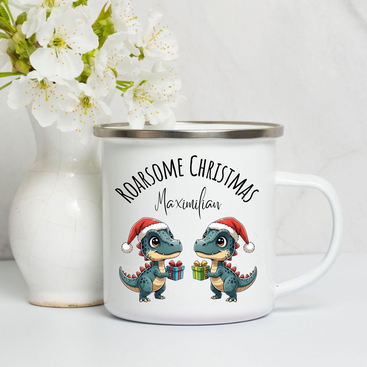 Personalisierte Emaille Weihnachtstasse für Kinder mit Namen und Dinosaurier. Zwei Dinos mit Weihnachtsmützen und Geschenken sorgen für festliche Stimmung. Diese bruchsichere Kindertasse aus Emaille ist leicht, robust und ideal für kleine Hände. Perfekt als Kakao-Tasse im Advent, Weihnachtsgeschenk für Kinder, Nikolaus-Mitbringsel oder festliches Accessoire. Ideal für kleine Dino-Fans, Kindergartenkinder oder den Adventskalender. Emailletasse mit Weihnachtsmotiv, personalisierbar mit Wunschnamen