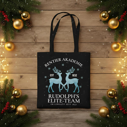 Weihnachtliche Stofftasche mit Rentier-Motiv „Rentier Akademie – Rudolph’s Elite-Team“ im Vintage-Stil. Ideale Baumwolltasche für Weihnachten, Einkäufe, Geschenke oder als nachhaltiger Jutebeutel. Perfekt als Geschenkidee oder als wiederverwendbare Geschenktasche mit Weihnachtsdesign. Waschbar, langlebig, mit langen Henkeln – als Weihnachtsgeschenktasche, Stoffbeutel oder Einkaufstasche nutzbar. Ideal für Damen, Herren oder Kinder zur Weihnachtszeit. Farben: Natur, Blau, Schwarz.