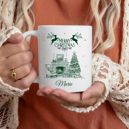 Weiße Keramiktasse mit festlichem Weihnachtsmotiv: Kamin mit festlich geschmücktem Weihnachtsbaum, Geschenken und einem eleganten Sessel. Darüber steht "Merry Christmas", begleitet von Rentier-Silhouetten. Unten ist ein Name personalisiert – in diesem Beispiel "Marie". Ideal als personalisiertes Weihnachtsgeschenk für Freund, Freundin, Partner oder Familienmitglied. Perfekt als Tasse für die Adventszeit, Nikolaus, Wichtelgeschenk oder als dekoratives Lieblingsstück für gemütl