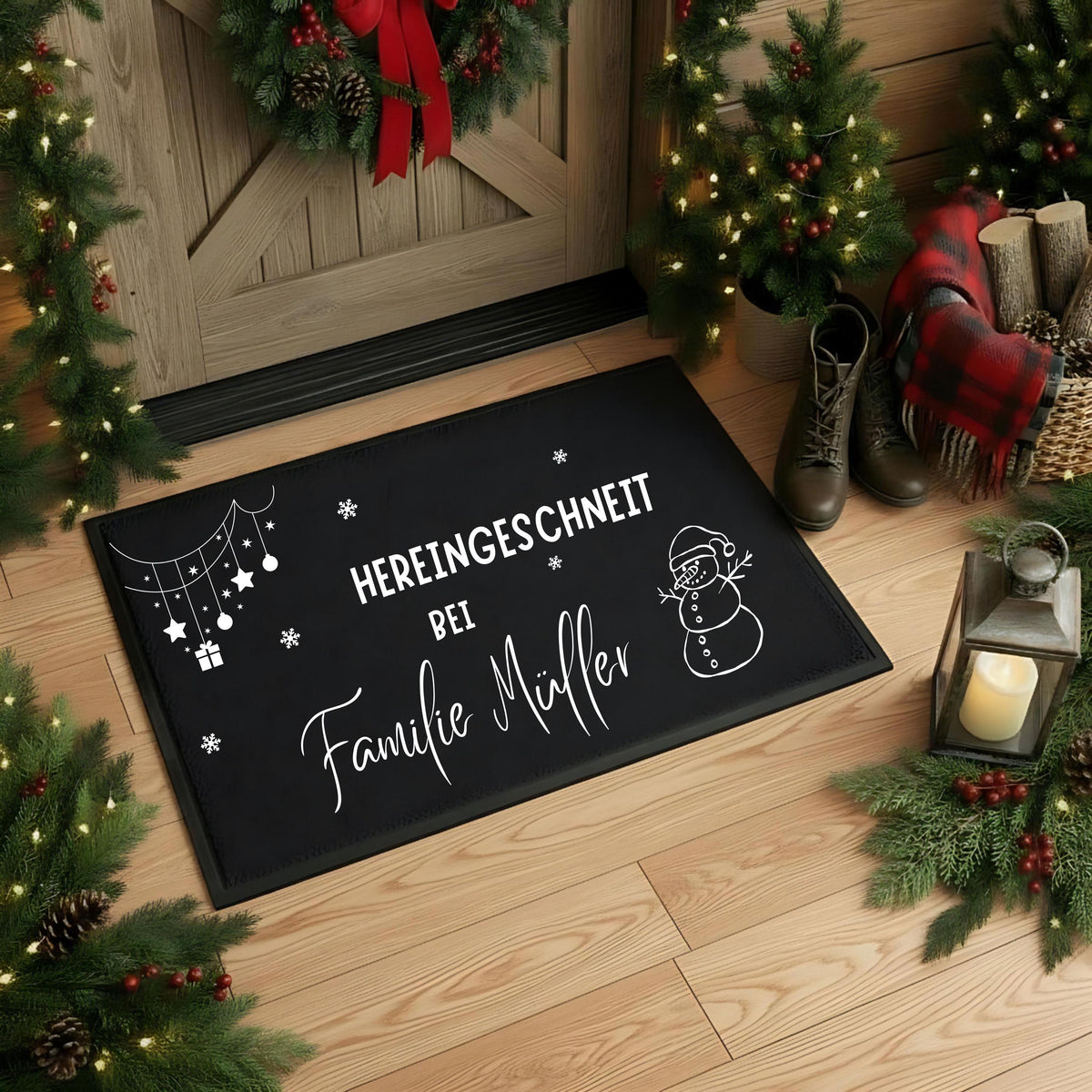 Schwarze Weihnachtsfußmatte mit weißer Personalisierung „Hereingeschneit bei Familie Müller“, Schneeflocken, Schneemann mit Mütze sowie hängenden Sternen, Kugeln und Geschenk. Die rechteckige Türmatte liegt schräg auf hellen Holzdielen vor einer naturfarbenen Holztür mit Weihnachtskranz und roter Schleife. Beleuchtete Tannenbäume, Zweige mit roten Beeren, Stiefel, eine karierte Decke, Holzscheite und eine Kerzenlaterne rahmen die Szene ein. Die lesbare Namensgestaltung zeigt ein Beispiel für den Wunschtext.