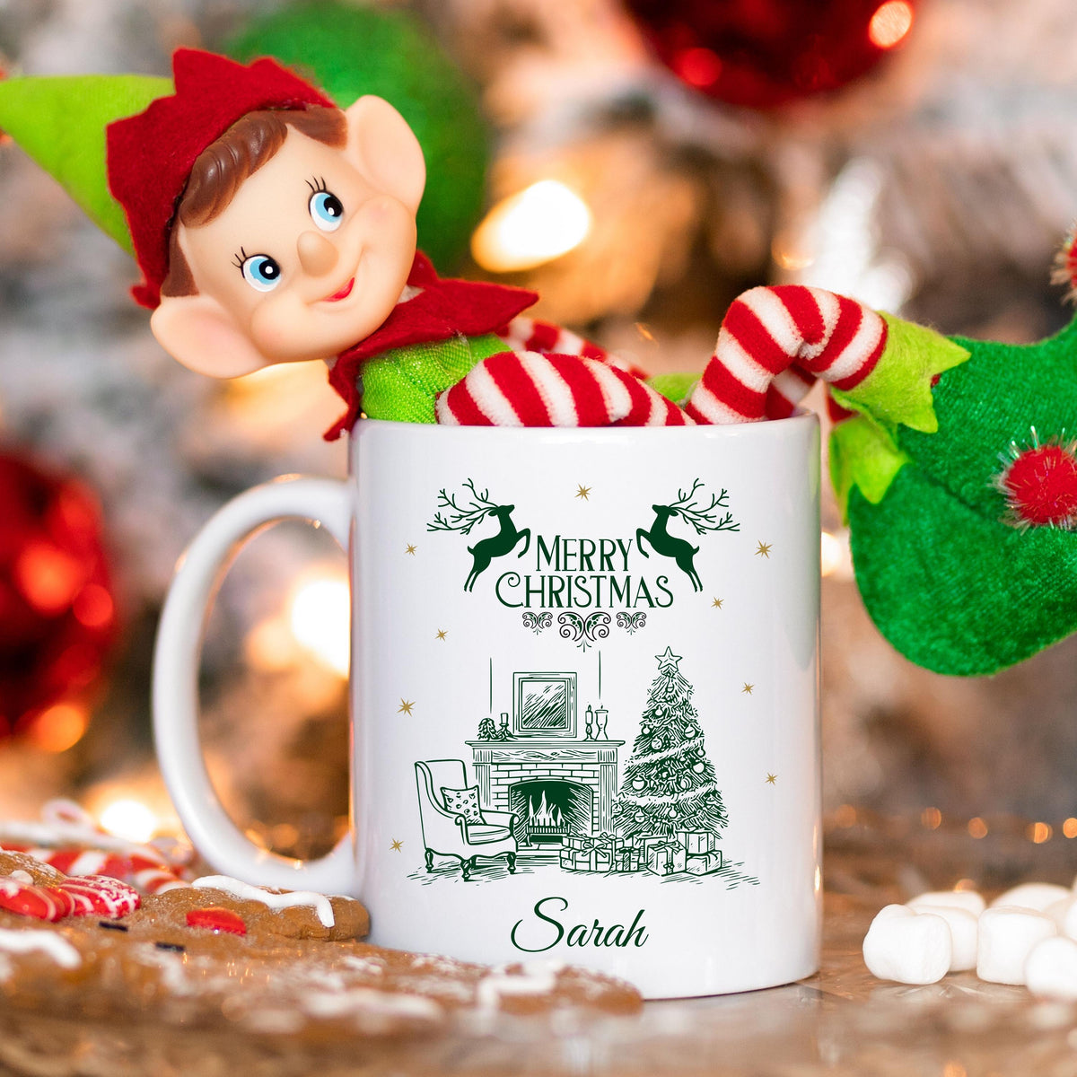 Weiße Keramiktasse mit festlichem Weihnachtsmotiv: Kamin mit festlich geschmücktem Weihnachtsbaum, Geschenken und einem eleganten Sessel. Darüber steht "Merry Christmas", begleitet von Rentier-Silhouetten. Unten ist ein Name personalisiert – in diesem Beispiel "Marie". Ideal als personalisiertes Weihnachtsgeschenk für Freund, Freundin, Partner oder Familienmitglied. Perfekt als Tasse für die Adventszeit, Nikolaus, Wichtelgeschenk oder als dekoratives Lieblingsstück für gemütl