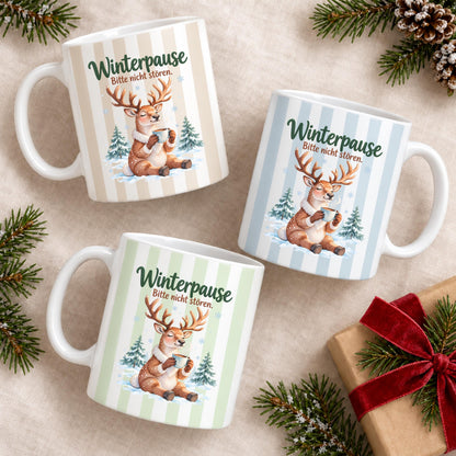 Weihnachtstasse mit dem Spruch „Winterpause, Bitte nicht stören" zeigt drei Varianten dieser Keramiktasse Weihnachten in Beige, Grün und Blau mit zartem Streifendesign. Auf jeder Kaffeetasse Weihnachten liegt ein schläfriges Rentier im Schnee zwischen kleinen Tannen und hält eine dampfende Tasse in den Pfoten. Diese Winter Tasse Geschenk eignet sich als Wichtelgeschenk Tasse, Weihnachtsgeschenk Tasse oder Weihnachtsbecher Geschenk und ist rundherum mit dem winterlichen Motiv bedruckt.