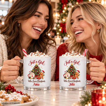 Zwei Freundinnen halten personalisierte Weihnachtstassen aus satiniertem Glas mit den Beispielnamen Anna und Julia. Das Motiv „Just a Girl Who Loves Christmas“ zeigt einen geschmückten Tannenbaum, Kakao mit Zuckerstange, Lebkuchenmann und Geschenke. Die Glastassen sind mit Sahne und Zuckerstangen angerichtet, im Hintergrund leuchten Weihnachtsbaum und Kerzen. Die 300-ml-Tasse mit Wunschname ist eine Geschenkidee für Freundin, Schwester oder Kollegin zu Weihnachten, Nikolaus und zum Wichteln.