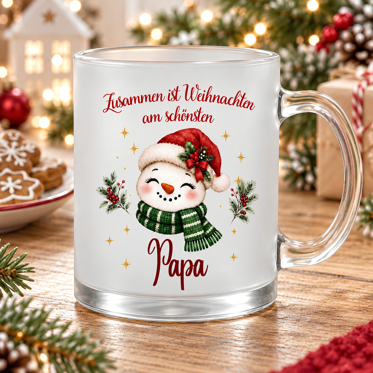 Personalisierte Weihnachtstasse für Papa aus satiniertem Glas mit transparentem Henkel rechts. Ein Schneemann mit Karottennase trägt eine rote Nikolausmütze, eine Beerenschleife und einen grün-weiß gestreiften Schal. Goldene Sterne und Tannenzweige umrahmen das Motiv unter dem roten Spruch „Zusammen ist Weihnachten am schönsten“. Der Name Papa steht darunter in roter Schreibschrift. Die Glastasse steht auf Holz vor Lichtern, Weihnachtsplätzchen, Geschenken und Tannengrün als Geschenk für den Vater.
