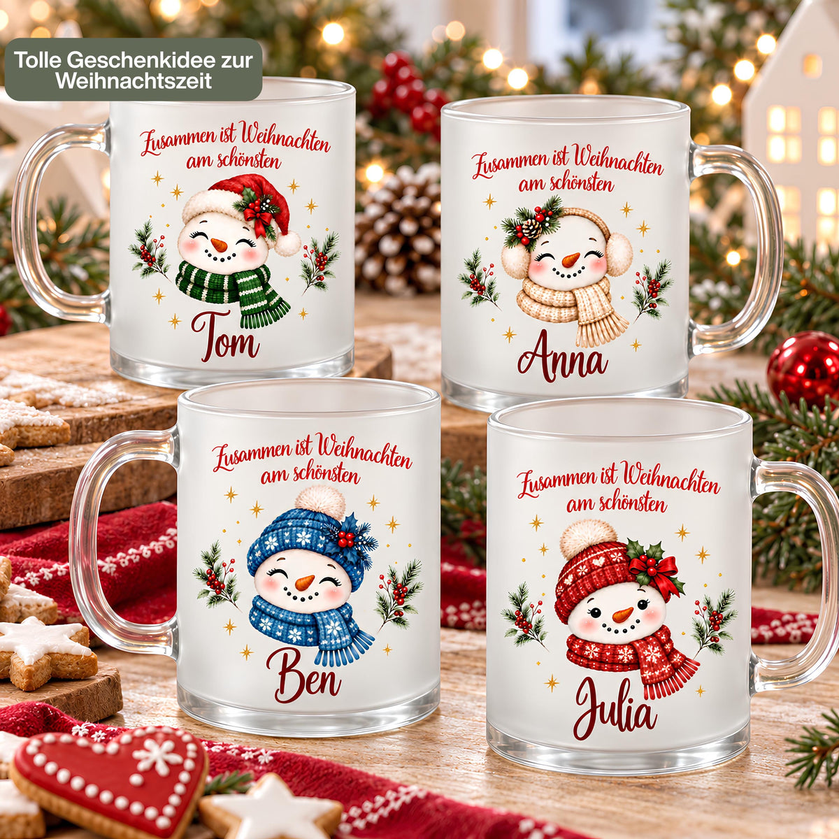 Vier personalisierte Weihnachtstassen aus satiniertem Glas mit Schneemann-Motiven und Namen: Tom trägt Nikolausmütze und grünen Schal, Anna beige Ohrenschützer, Ben blaue Mütze und Schal und Julia ein rotes Set. Über jedem Motiv steht „Zusammen ist Weihnachten am schönsten“. Die Glastassen mit transparenten Henkeln stehen auf einem Holztisch zwischen Weihnachtsplätzchen, rotem Strickstoff, Tannengrün und Christbaumkugeln. Warme Lichter und ein Dekohaus begleiten die Geschenkidee für Familie und Freunde.