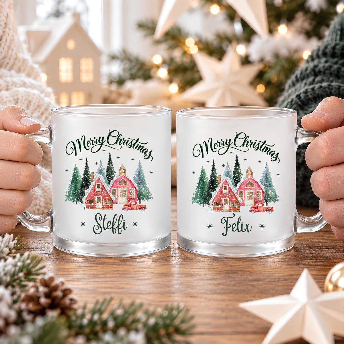 Zwei personalisierte Weihnachtstassen mit den Namen Steffi und Felix, nebeneinander in Händen gehalten. Satinierte Glastassen mit Merry Christmas Schriftzug und rotem Winterdorf zwischen grünen Tannen. Die Tasse mit Wunschname ist eine persönliche Geschenkidee zu Weihnachten für Partner, Mama, Papa oder Freunde. Weihnachtsbecher mit ca. 300 ml für Kaffee, Tee, Kakao und Glühwein, passend für gemeinsame Genussmomente im Advent und als individuelles Nikolausgeschenk oder Wichtelgeschenk. Höhe ca. 95 mm.