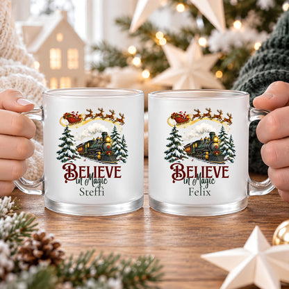 Zwei personalisierte Weihnachtstassen mit den Namen Steffi und Felix, an den Glashenkeln gehalten. Believe in Magic Schriftzug mit Weihnachtsbahn und Weihnachtsmann auf satiniertem Glas. Die Tasse mit Wunschname ist eine Weihnachtsgeschenkidee für Partner, Mama, Papa oder Freunde. Weihnachtsbecher mit ca. 300 ml für Kaffee, Tee, Kakao oder Glühwein und gemeinsame Momente im Advent. Individuell bedruckte Kaffeetasse als Nikolausgeschenk, Wichtelgeschenk oder Geschenk für Weihnachtsfans.