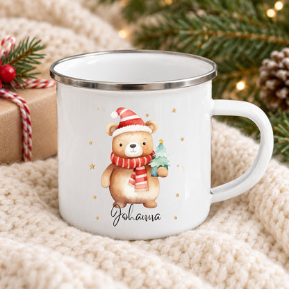 Personalisierte Weihnachtstasse für Kinder aus weißer Emaille mit silberfarbenem Rand und weißem Henkel. Das Motiv zeigt einen braunen Weihnachtsbären mit roter Weihnachtsmütze, rot-weiß gestreiftem Schal und einem grünen Tannenbaum im Arm. Unter dem Bären steht ein Beispielname; die Kindertasse wird mit Wunschname bedruckt. Weihnachtsbecher für Bärenfans und eine Geschenkidee zu Weihnachten oder Nikolaus für Kinder, Enkelkinder und Patenkinder. Nahansicht von Weihnachtsbär und Namensdruck.