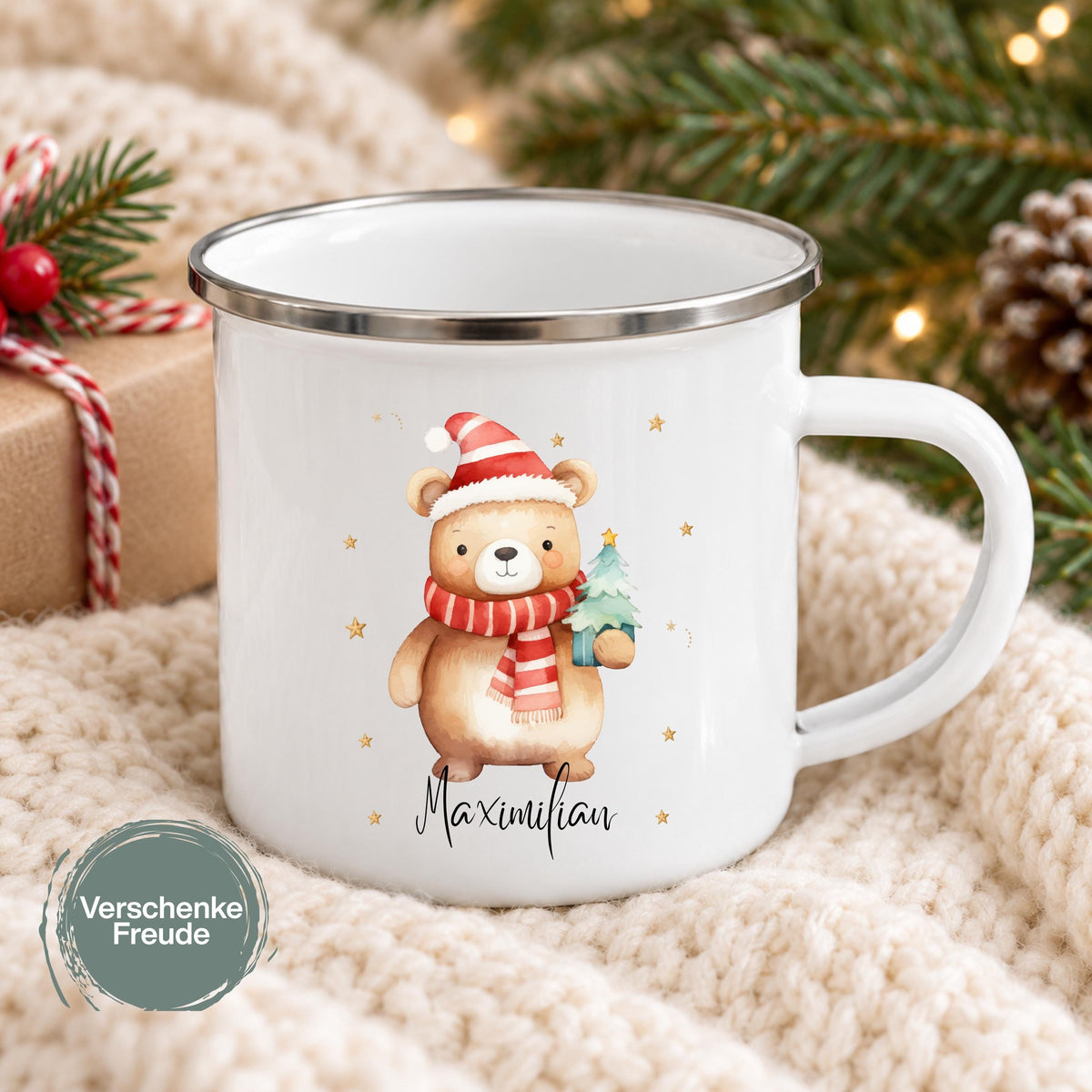 Personalisierte Weihnachtstasse für Kinder aus weißer Emaille mit silberfarbenem Rand und weißem Henkel. Das Motiv zeigt einen braunen Weihnachtsbären mit roter Weihnachtsmütze, rot-weiß gestreiftem Schal und einem grünen Tannenbaum im Arm. Unter dem Bären steht ein Beispielname; die Kindertasse wird mit Wunschname bedruckt. Weihnachtsbecher für Bärenfans und eine Geschenkidee zu Weihnachten oder Nikolaus für Kinder, Enkelkinder und Patenkinder. Frontansicht mit personalisiertem Namensdruck.