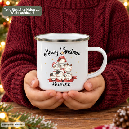 Personalisierte Weihnachtstasse für Kinder aus weißer Emaille mit silberfarbenem Rand und weißem Henkel. Sechs Katzen mit verschiedenen Fellfarben und Weihnachtsaccessoires bilden das Motiv unter dem Schriftzug „Meowy Christmas“. Darunter steht ein Beispielname; die Kindertasse wird mit Wunschname bedruckt. Persönlicher Weihnachtsbecher für Katzenfans und eine Geschenkidee zu Weihnachten oder Nikolaus für Kinder, Enkelkinder und Patenkinder. Eine Person hält die Tasse mit beiden Händen.