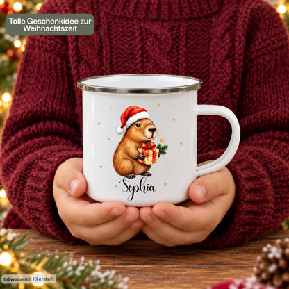 Personalisierte Weihnachtstasse für Kinder aus weißer Emaille mit silberfarbenem Rand und weißem Henkel. Das Weihnachtsmotiv zeigt ein Capybara mit roter Weihnachtsmütze und einem Geschenk mit roter Schleife. Unter dem Tiermotiv steht ein Beispielname; die Kindertasse wird mit Wunschname bedruckt. Persönlicher Weihnachtsbecher für Capybara-Fans und eine Geschenkidee zu Weihnachten oder Nikolaus für Kinder, Enkelkinder und Patenkinder. Ansicht der Tasse in den Händen einer Person.