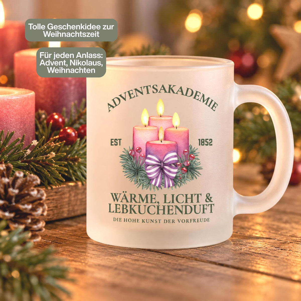 Weihnachtsbecher Adventsakademie aus satiniertem Glas mit vier rosa Adventskerzen und gestreifter Schleife im Tannengrün. Die Vorderansicht zeigt den Schriftzug „Wärme, Licht & Lebkuchenduft“ und „Die hohe Kunst der Vorfreude“, ergänzt durch „EST 1852“. Diese beidseitig bedruckte Glastasse mit Henkel fasst ca. 300 ml. Sie eignet sich als Wichtelgeschenk für Kollegen, Weihnachtsgeschenk für eine Freundin oder Nikolausgeschenk und begleitet Kaffee, Tee, Kakao oder Glühwein im Advent.