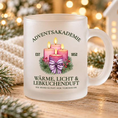 Nahansicht der satinierten Glastasse mit dem Adventsakademie-Motiv: vier rosa Kerzen, Tannengrün und gestreifte Schleife. „Wärme, Licht & Lebkuchenduft“ und „Die hohe Kunst der Vorfreude“ stehen unter dem Kerzenmotiv; darüber ist „Adventsakademie“ zu lesen. Der beidseitig bedruckte Weihnachtsbecher mit Henkel fasst ca. 300 ml. Als Tasse für Kaffee, Tee, Kakao oder Glühwein begleitet er die Adventszeit. Passend als Weihnachtsgeschenk, Nikolaus-Aufmerksamkeit oder Wichtelgeschenk für Freunde.