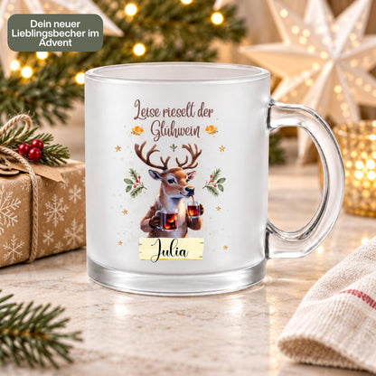 Personalisierte Glühweintasse mit Namen und dem Spruch „Leise rieselt der Glühwein" zeigt diese transparente, satinierte Glastasse mit einem Rentier, das zwei Gläser Glühwein hält, umgeben von Tannengrün und Sternen. Diese Tasse personalisiert wird mit dem Wunschnamen auf einem kleinen Schild bedruckt. Diese Weihnachtstasse mit Namen eignet sich als Weihnachtsgeschenk-Tasse für Mama, Papa oder die ganze Familie und macht aus jeder Glühweintasse ein persönliches Unikat für die Adventszeit.
