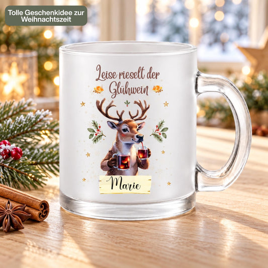 Personalisierte Glühweintasse mit Namen und dem Spruch „Leise rieselt der Glühwein" zeigt diese transparente, satinierte Glastasse mit einem Rentier, das zwei Gläser Glühwein hält, umgeben von Tannengrün und Sternen. Diese Tasse personalisiert wird mit dem Wunschnamen auf einem kleinen Schild bedruckt. Diese Weihnachtstasse mit Namen eignet sich als Weihnachtsgeschenk-Tasse für Mama, Papa oder die ganze Familie und macht aus jeder Glühweintasse ein persönliches Unikat für die Adventszeit.