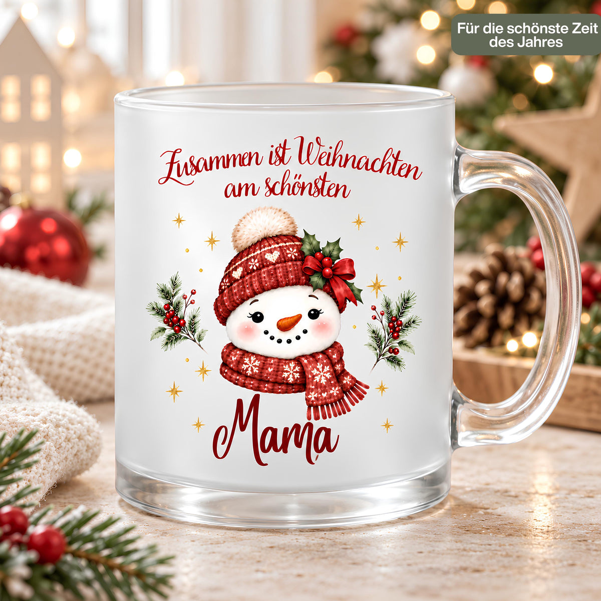Personalisierte Weihnachtstasse für Mama aus satiniertem Glas mit transparentem Henkel rechts. Der Schneemann trägt rote Strickmütze und Schal mit weißen Schneeflocken sowie eine Schleife aus roten Beeren und grünen Blättern. Goldene Sterne und Tannenzweige umrahmen das Motiv; darüber steht „Zusammen ist Weihnachten am schönsten“, darunter Mama in roter Schreibschrift. Die Glastasse steht auf Holz neben weißem Strickstoff, Christbaumkugeln und Zapfen. Ein Schild nennt „Für die schönste Zeit des Jahres“.