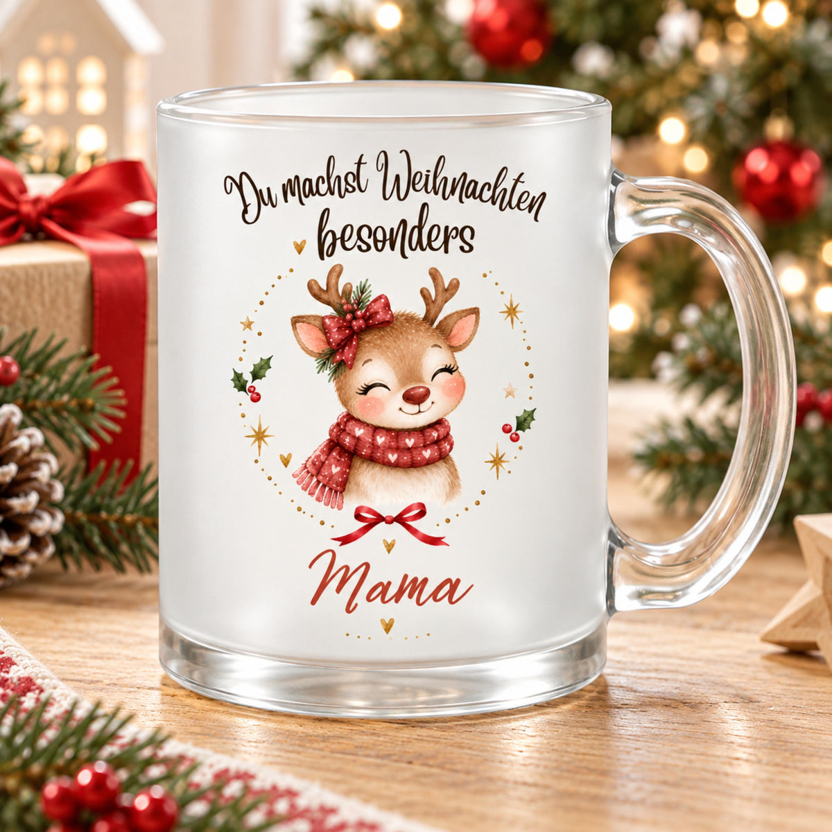Personalisierte Weihnachtstasse für Mama aus satiniertem Glas mit Rentier und transparentem Henkel rechts. Das Rentier trägt einen roten Herzschal und eine rote Schleife am Geweih, ergänzt durch Tannengrün. Goldene Sterne, Herzen und Beerenzweige umrahmen das Motiv unter „Du machst Weihnachten besonders“. Mama steht darunter in Rot. Auf dem Holztisch begleiten Geschenke mit rotem Band, Zapfen, Tannenzweige und ein Holzstern die Tasse; der Weihnachtsbaum leuchtet im Hintergrund. Geschenk für die Mutter.