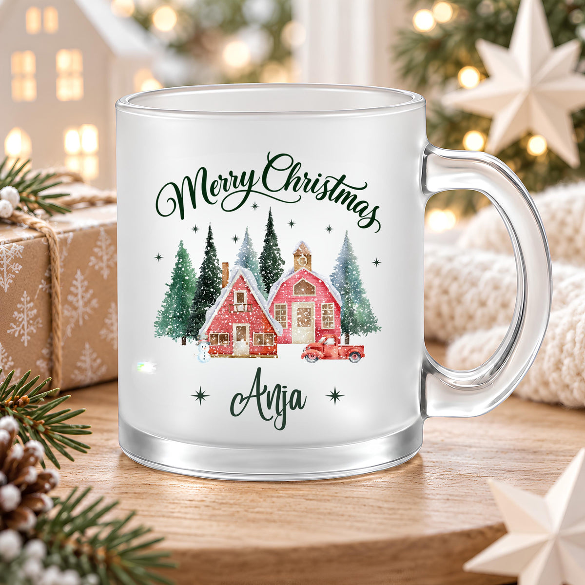 Personalisierte Weihnachtstasse mit Namen Anja auf einem Holztisch in weihnachtlicher Umgebung. Satinierte Glastasse mit transparentem Henkel, Merry Christmas Schriftzug und rotem Winterdorf mit Tannen. Der Weihnachtsbecher mit Wunschname fasst ca. 300 ml für Kaffee, Tee, Kakao oder Glühwein. Persönliche Geschenkidee zu Weihnachten für Mama, Oma, Schwester oder Freundin, als Nikolausgeschenk oder zum Wichteln. Eine individuell bedruckte Tasse für gemütliche Kaffeemomente in der Adventszeit. Höhe ca. 95 mm.