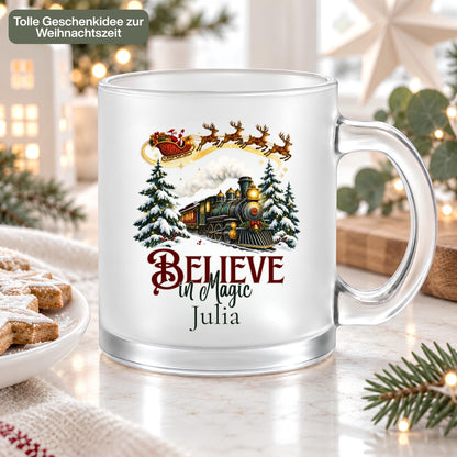 Personalisierte Weihnachtstasse mit Namen Julia und Believe in Magic Schriftzug. Weihnachtsbahn und Weihnachtsmann im Rentierschlitten schmücken den beidseitig bedruckten Weihnachtsbecher aus satiniertem Glas. Die Tasse mit Wunschname fasst ca. 300 ml für Kaffee, Tee, Kakao oder Glühwein. Weihnachtsgeschenk für die beste Freundin, Mama, Oma, Schwester oder Kollegin. Eine individuelle Kaffeetasse als Nikolausgeschenk, Wichtelgeschenk und Geschenkidee für die Adventszeit und Weihnachten.