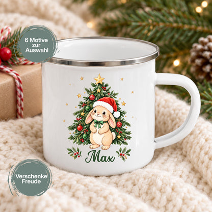 Personalisierte Weihnachtstasse für Kinder aus weißer Emaille mit silberfarbenem Rand und weißem Henkel. Das Motiv zeigt einen Hasen mit roter Weihnachtsmütze und grüner Schleife vor einem geschmückten Tannenbaum; darunter steht der Beispielname Max. Kinderbecher mit Wunschname als Weihnachtsgeschenk oder Nikolausgeschenk für Kinder, Enkelkinder und Patenkinder. Eine Tasse im gewählten Design, ca. 300 ml. Gezeigt auf einer hellen Decke mit Tannenzweigen und Geschenk; sechs Tiermotive stehen zur Auswahl.