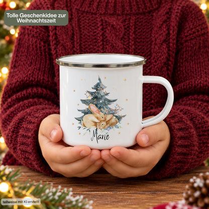Personalisierte Weihnachtstasse für Kinder aus weißer Emaille mit silberfarbenem Rand und weißem Henkel. Das Hasenmotiv zeigt zwei braune Hasen unter einem geschmückten Weihnachtsbaum. Unter der winterlichen Illustration steht ein Beispielname; die Kindertasse wird mit Wunschname bedruckt. Persönlicher Weihnachtsbecher für kleine Hasenfans und eine Geschenkidee zu Weihnachten oder Nikolaus für Kinder, Enkelkinder und Patenkinder. Eine Person zeigt die bedruckte Emaille-Tasse.