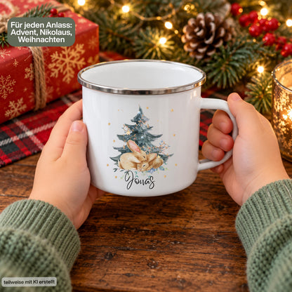 Personalisierte Weihnachtstasse für Kinder aus weißer Emaille mit silberfarbenem Rand und weißem Henkel. Das Hasenmotiv zeigt zwei braune Hasen unter einem geschmückten Weihnachtsbaum. Unter der winterlichen Illustration steht ein Beispielname; die Kindertasse wird mit Wunschname bedruckt. Persönlicher Weihnachtsbecher für kleine Hasenfans und eine Geschenkidee zu Weihnachten oder Nikolaus für Kinder, Enkelkinder und Patenkinder. Die Tasse wird mit beiden Händen gehalten.